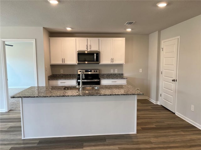 kitchen with white cabinets, dark wood-type flooring, stove, and a center island with sink