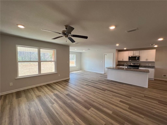 kitchen with ceiling fan, hardwood / wood-style floors, a center island with sink, white cabinetry, and appliances with stainless steel finishes