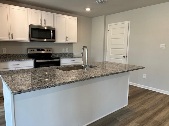 kitchen with dark hardwood / wood-style flooring, dark stone counters, stainless steel appliances, an island with sink, and sink