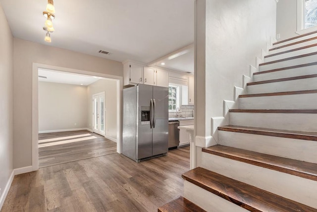 kitchen featuring sink, tasteful backsplash, appliances with stainless steel finishes, white cabinets, and hardwood / wood-style flooring