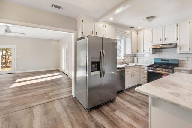 kitchen featuring white cabinetry, stainless steel appliances, light stone counters, backsplash, and light wood-type flooring