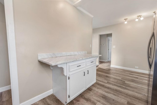 kitchen featuring kitchen peninsula, stainless steel fridge, light stone countertops, crown molding, and white cabinetry