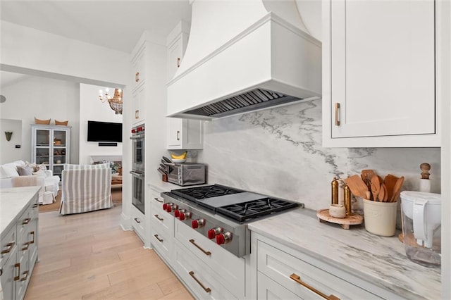 kitchen featuring white cabinetry, light hardwood / wood-style floors, appliances with stainless steel finishes, and premium range hood