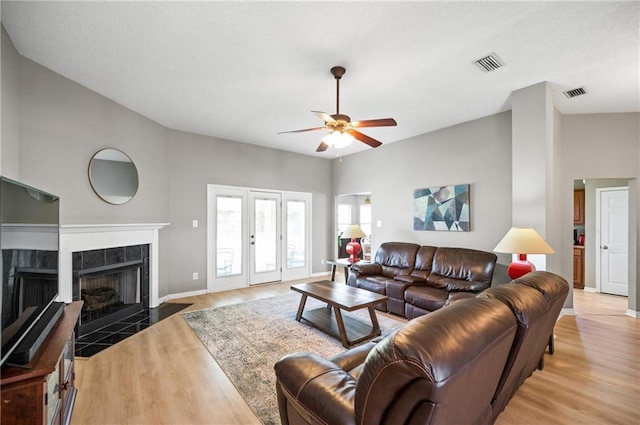 living room with ceiling fan, a tiled fireplace, and light hardwood / wood-style floors