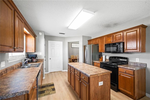 kitchen with sink, a textured ceiling, black appliances, a center island, and light wood-type flooring