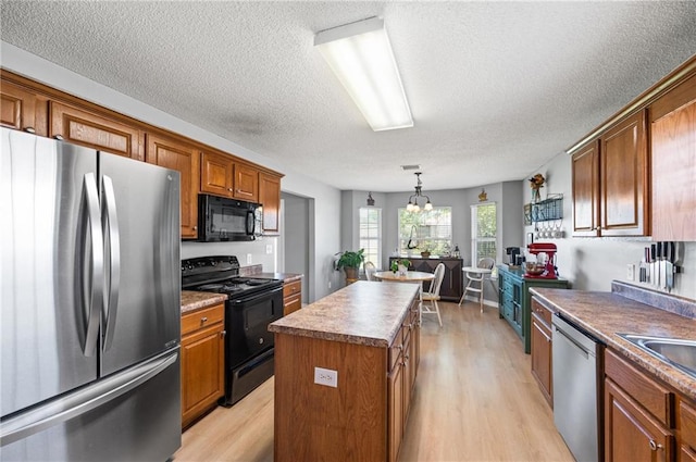 kitchen with pendant lighting, a textured ceiling, light hardwood / wood-style flooring, black appliances, and a center island