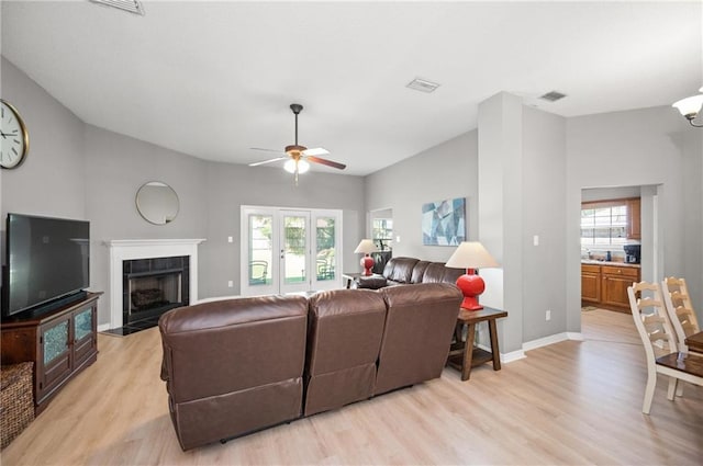 living room with ceiling fan, a tiled fireplace, light hardwood / wood-style floors, and a healthy amount of sunlight