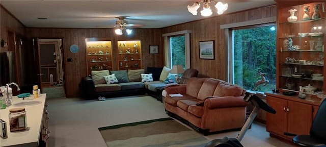 carpeted living room featuring wooden walls, sink, and ceiling fan with notable chandelier