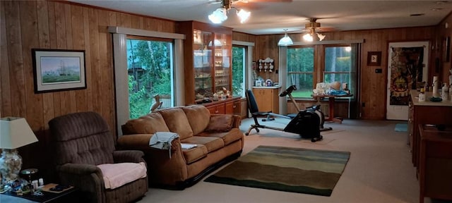 living area featuring ceiling fan, light colored carpet, and wood walls