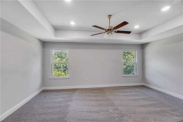 carpeted empty room with ceiling fan, a tray ceiling, and a wealth of natural light