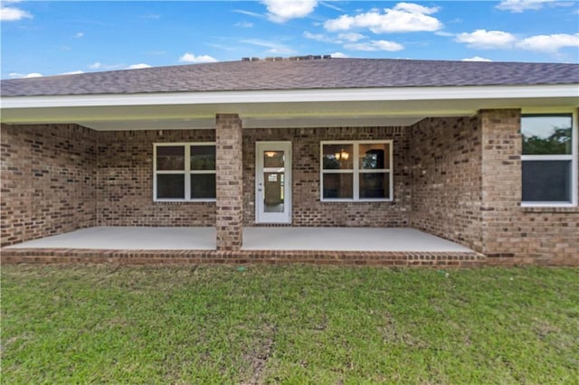 doorway to property with a lawn, brick siding, and a patio area