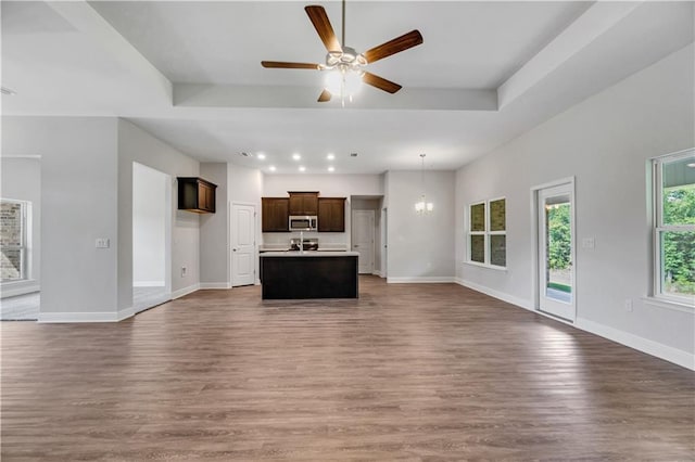 unfurnished living room with a raised ceiling, ceiling fan with notable chandelier, and hardwood / wood-style floors