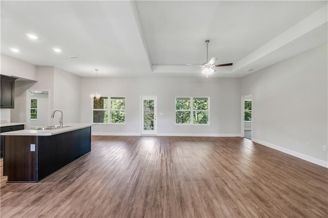 unfurnished living room with ceiling fan with notable chandelier, a raised ceiling, sink, and hardwood / wood-style floors