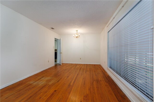 unfurnished room with a textured ceiling, hardwood / wood-style floors, and a chandelier