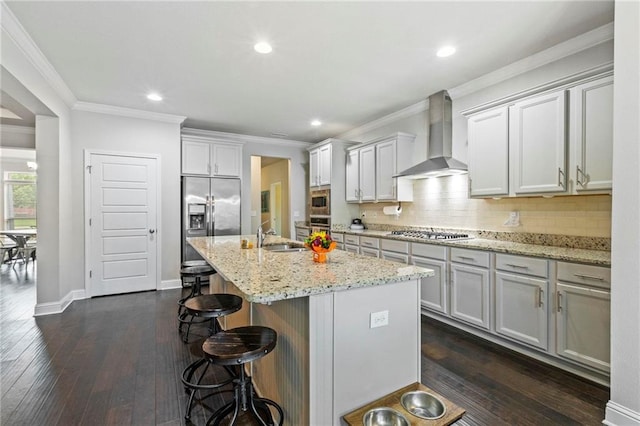 kitchen with built in appliances, dark hardwood / wood-style floors, wall chimney exhaust hood, a breakfast bar area, and a center island with sink