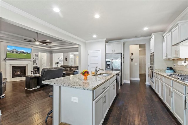 kitchen with a tiled fireplace, dark hardwood / wood-style flooring, an island with sink, sink, and ceiling fan