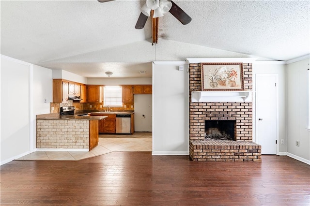 unfurnished living room with a textured ceiling, lofted ceiling with beams, light wood-type flooring, ceiling fan, and a brick fireplace