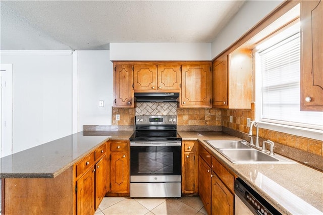 kitchen with a peninsula, a sink, brown cabinetry, under cabinet range hood, and appliances with stainless steel finishes