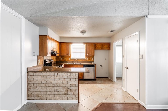 kitchen with brown cabinetry, stainless steel appliances, a peninsula, under cabinet range hood, and visible vents