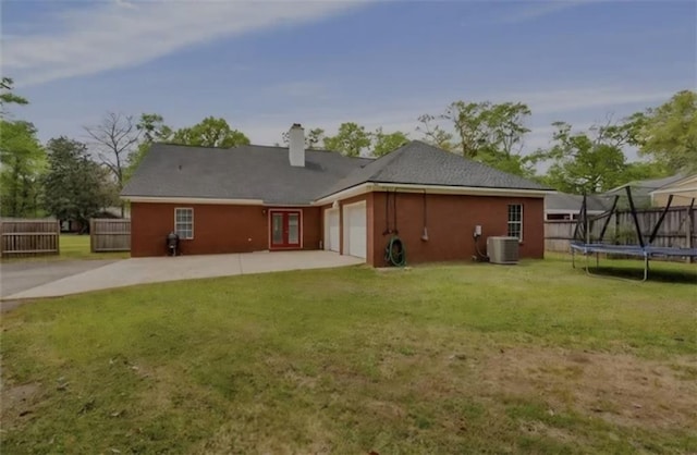 rear view of house featuring a trampoline, a lawn, central AC unit, fence, and a garage