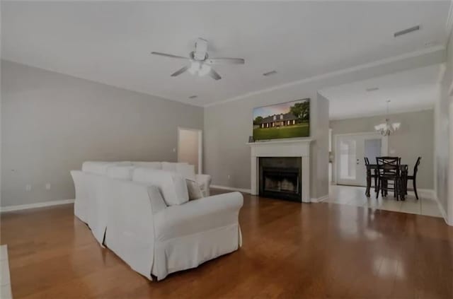 living area with ceiling fan with notable chandelier, a fireplace, baseboards, and wood finished floors