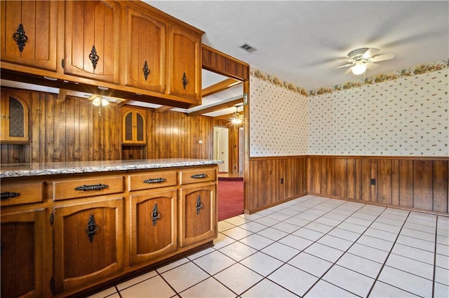 504 Vaughan Dr N, Satsuma, AL 36572 - kitchen featuring a ceiling fan, brown cabinets, wood walls, a wainscoted wall, and light tile patterned flooring