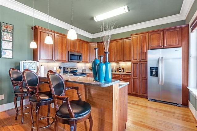 kitchen featuring kitchen peninsula, pendant lighting, stainless steel appliances, light wood-type flooring, and ornamental molding