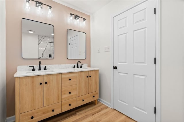 full bath featuring double vanity, wood finished floors, a sink, and baseboards