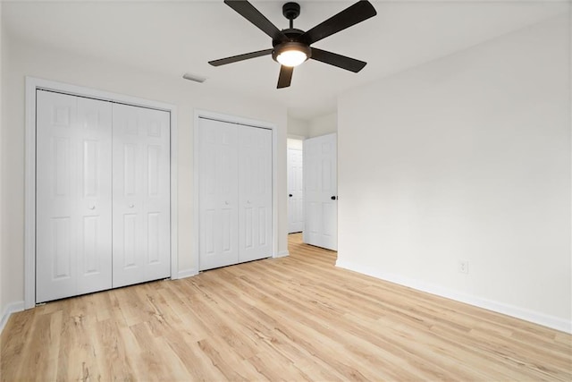 unfurnished bedroom with baseboards, visible vents, a ceiling fan, light wood-style flooring, and multiple closets