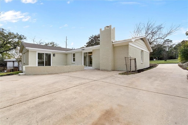 back of property with brick siding, driveway, and a chimney