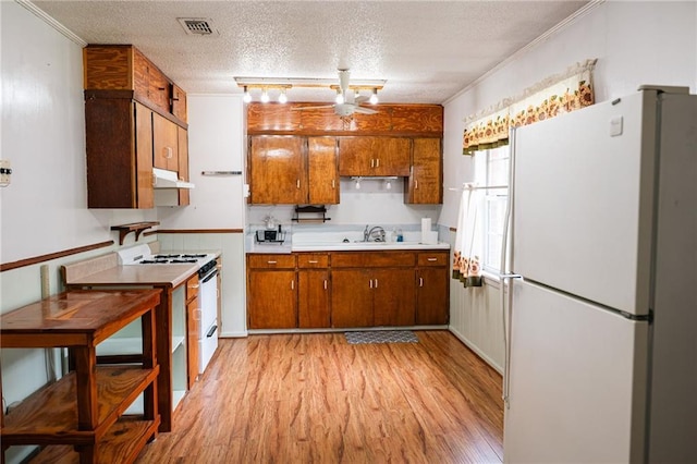 kitchen featuring white appliances, under cabinet range hood, light countertops, and brown cabinets