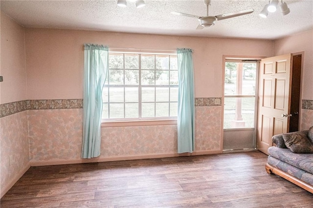 living area featuring a textured ceiling, wood finished floors, a ceiling fan, and wainscoting