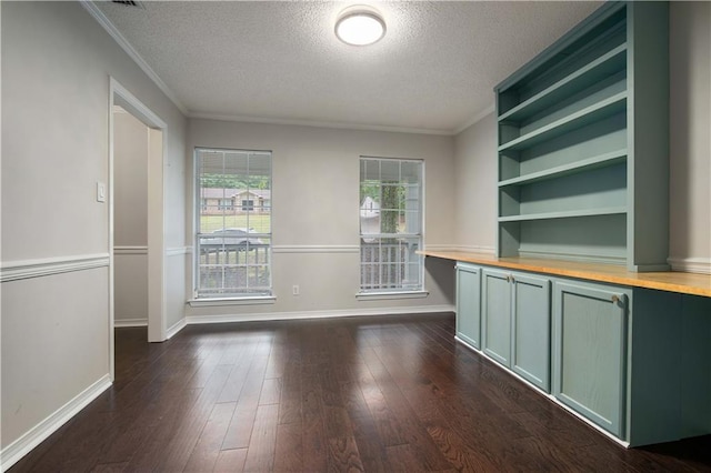 unfurnished dining area with baseboards, ornamental molding, a textured ceiling, and dark wood-type flooring