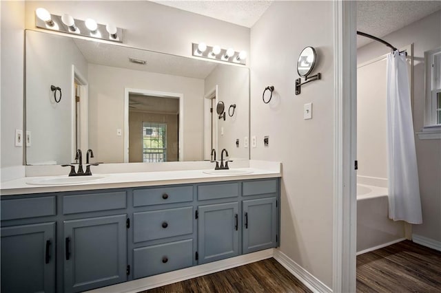 full bathroom featuring double vanity, a sink, a textured ceiling, and wood finished floors