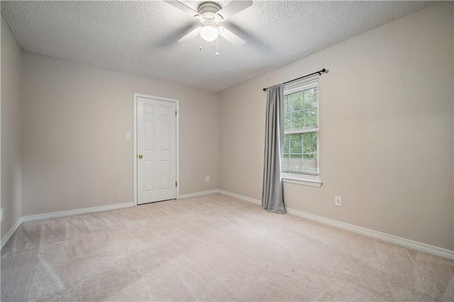 spare room featuring baseboards, light carpet, a ceiling fan, and a textured ceiling