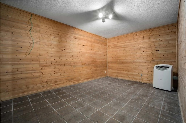 empty room featuring heating unit, a textured ceiling, wooden walls, and dark tile patterned flooring