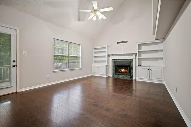 unfurnished living room featuring baseboards, ceiling fan, a lit fireplace, and dark wood finished floors