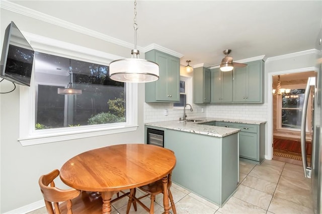 kitchen featuring hanging light fixtures, green cabinets, backsplash, sink, and light stone countertops