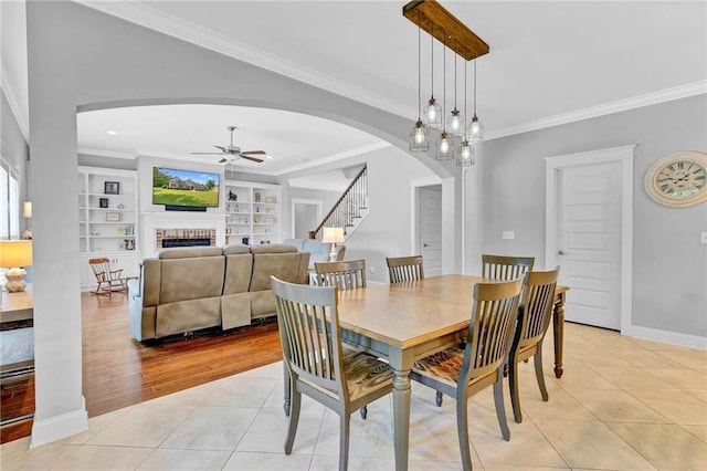 8662 Daintree Ct, Daphne, AL 36526 - dining room featuring arched walkways, a ceiling fan, ornamental molding, light tile patterned flooring, and a brick fireplace