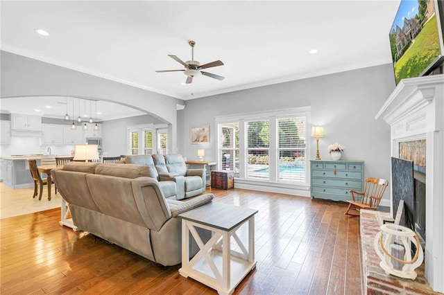 8662 Daintree Ct, Daphne, AL 36526 - living room with arched walkways, a ceiling fan, a fireplace with raised hearth, wood-type flooring, and ornamental molding