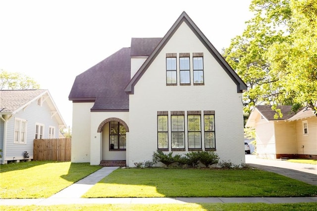 view of front facade with roof with shingles, fence, a front lawn, and brick siding
