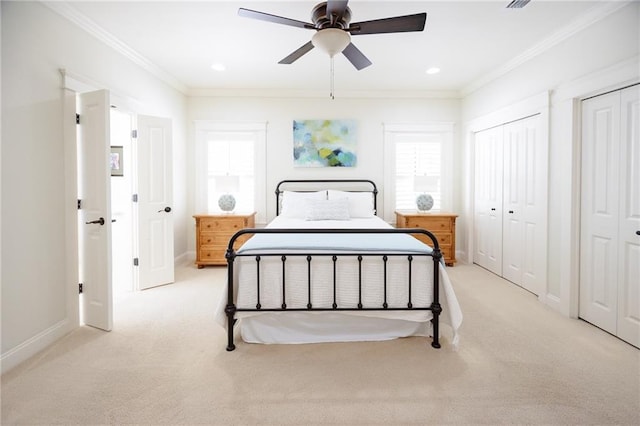 bedroom with crown molding, light carpet, and two closets