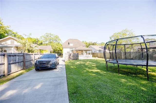 view of yard featuring concrete driveway, a trampoline, and a fenced backyard