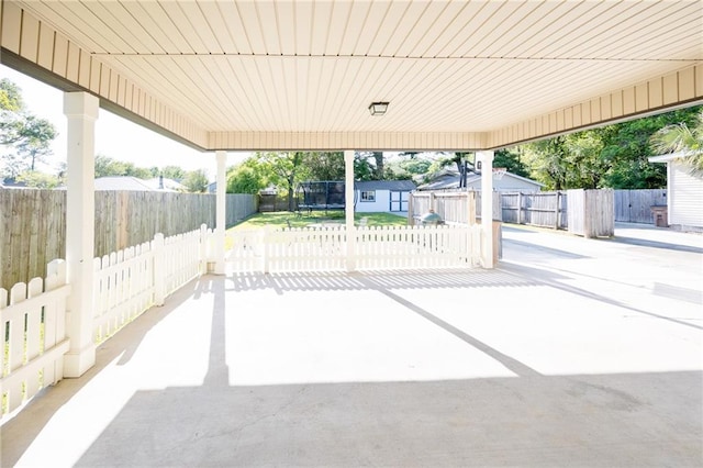 view of patio / terrace with a trampoline, a shed, an outbuilding, a fenced backyard, and an attached carport