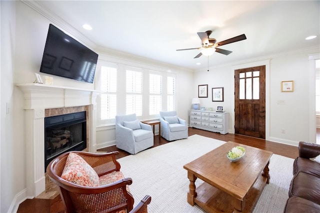 living room with a ceiling fan, ornamental molding, a fireplace, and wood finished floors