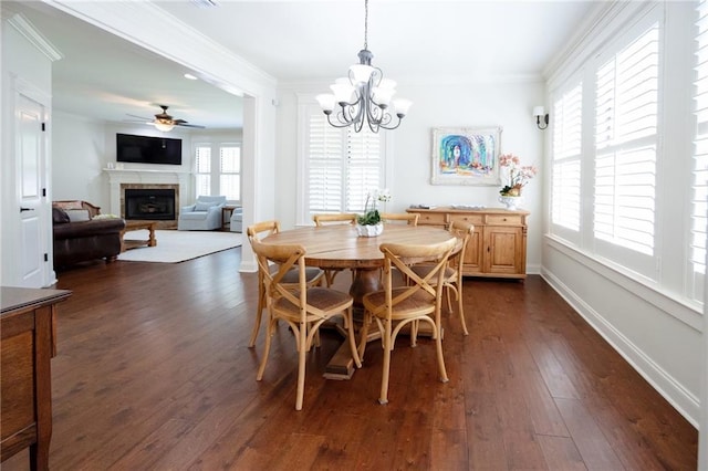 dining room with ceiling fan with notable chandelier, a fireplace, crown molding, dark wood-style flooring, and baseboards