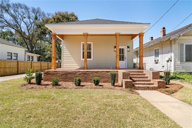 view of front facade with covered porch, a front yard, and fence