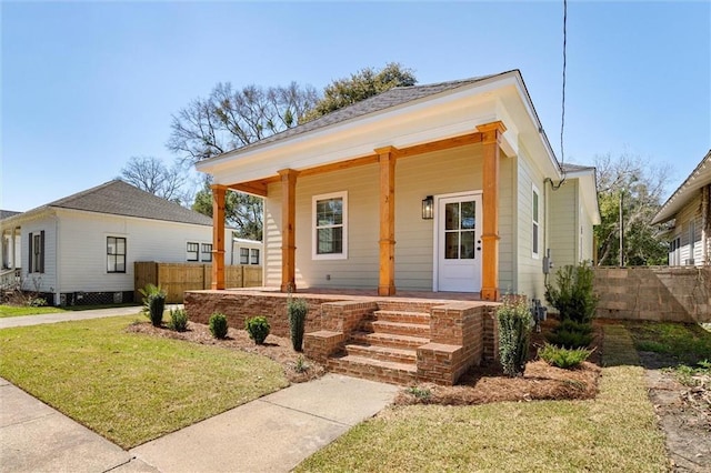 view of front of property featuring covered porch, a front yard, and fence