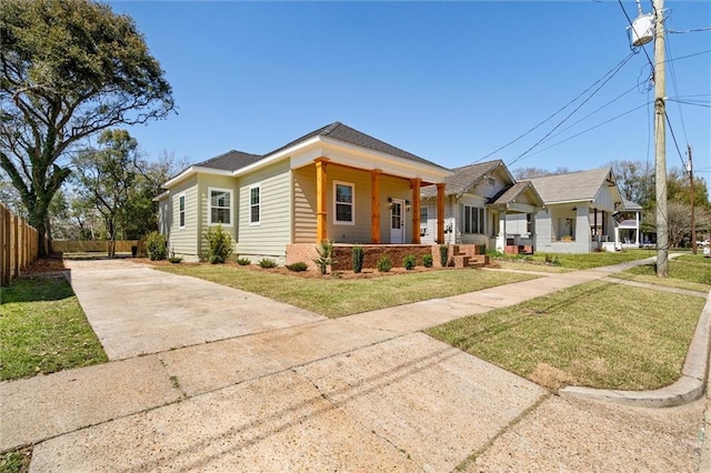 view of front of house with driveway, covered porch, a front yard, and fence