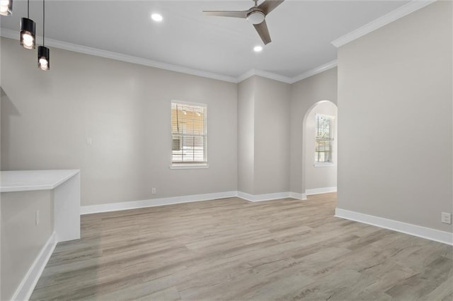 empty room with ceiling fan, baseboards, ornamental molding, light wood-style floors, and arched walkways